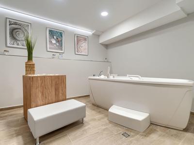 Moderner Hotelbadezimmer mit großer Badewanne, Hocker und dekorativer Pflanze.