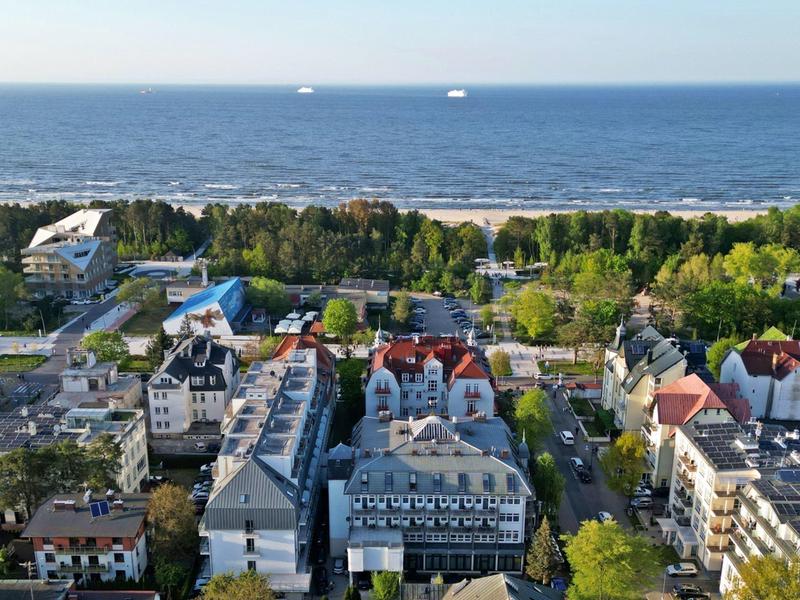 Blick auf ein Küstenstädtchen mit Wohnungen, Bäumen und Strand im Hintergrund.