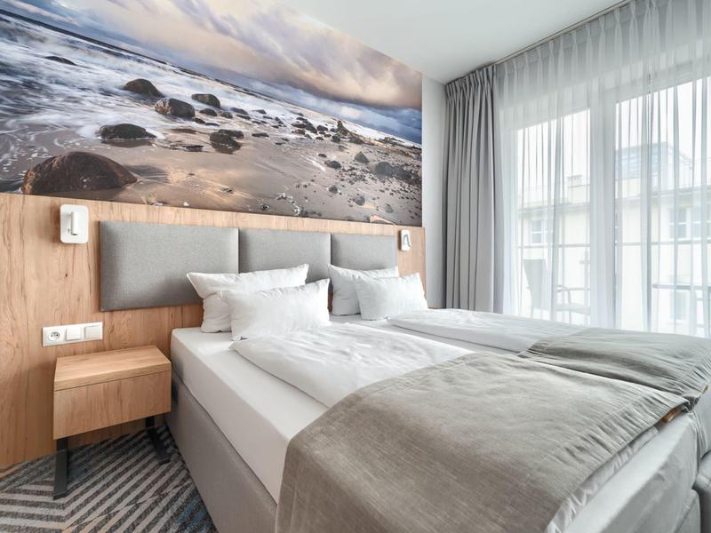 Modernes Hotelzimmer mit Doppelbett, Holzakzenten und großem Fenster mit hellen Vorhängen.