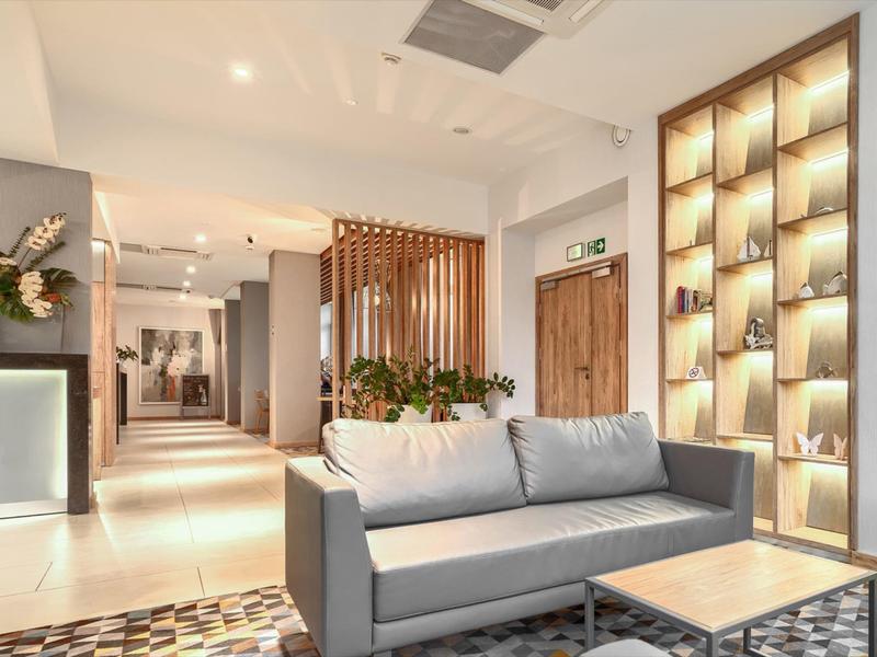 Moderne Hotel-Lounge mit grauem Sofa, Holzakzenten und dekorativer Beleuchtung.
