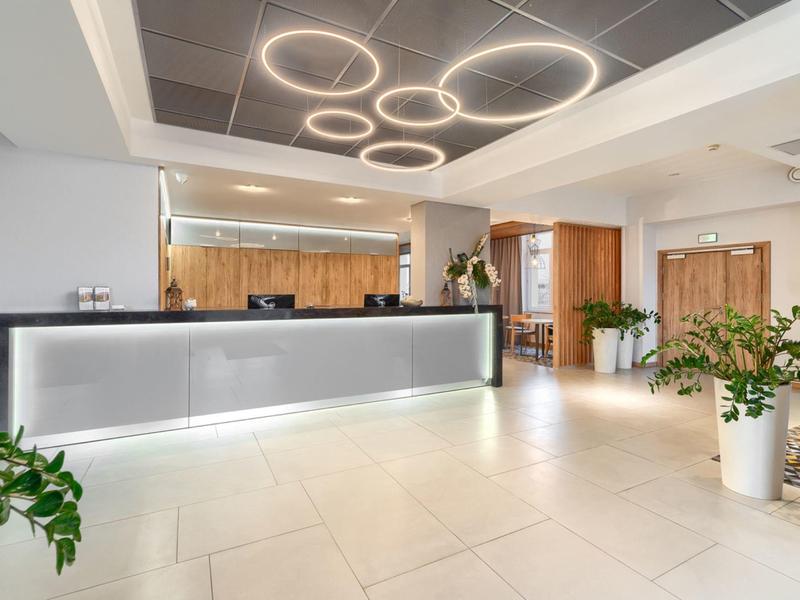 Moderner Hotel-Empfangsbereich mit beleuchtetem Tresen, Pflanzen und rundem Deckenlicht.