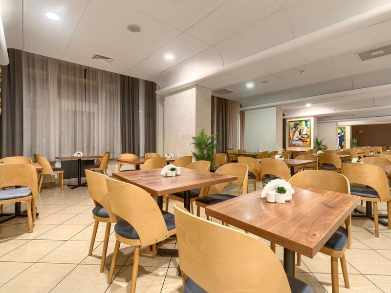 Moderner Frühstücksraum mit Holztischen, beigen Stühlen und gedeckten Tischen in einem Hotel.