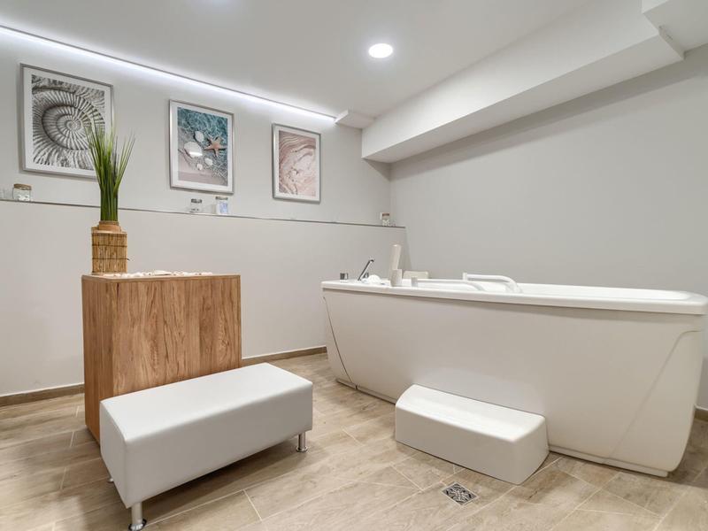 Moderner Hotelbadezimmer mit großer Badewanne, Hocker und dekorativer Pflanze.