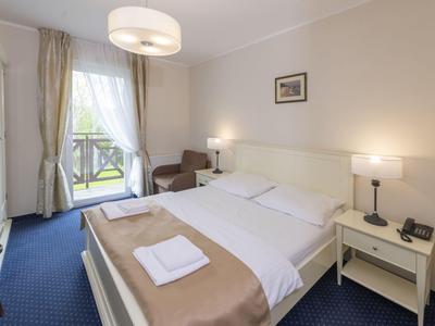 Hell eingerichtetes Hotelzimmer mit Doppelbett, zwei Nachttischen und Sessel neben Fenster.