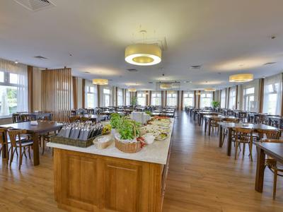 Moderner Speisesaal mit Holzboden, Tischen und Buffet in der Mitte.