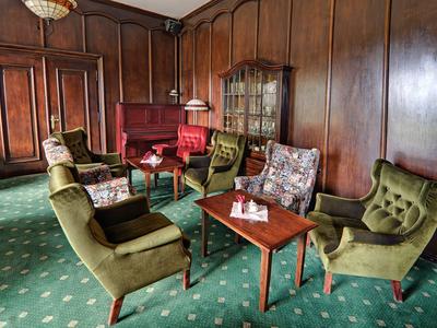 Eleganter Salon mit grünen Sesseln, roten Sofas und Holzvertäfelung an den Wänden.