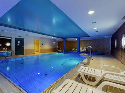 Basen kryty z niebieskim sufitem, leżakami i oknami w kształcie okręgów