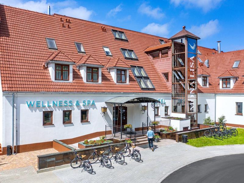 Nowoczesny budynek hotelowy z czerwonymi dachówkami, stojakami na rowery i przyległym trawnikiem.