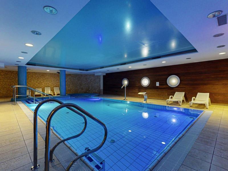 Wnętrze z oświetlonym basenem, drewnianymi panelami i leżakami.