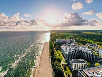 Luftaufnahme eines Hotels am Strand mit Sonnenuntergang und grünem Küstenwald.