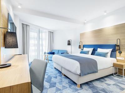 Nowoczesny pokój hotelowy z dużym łóżkiem, niebiesko-białymi akcentami i biurkiem.