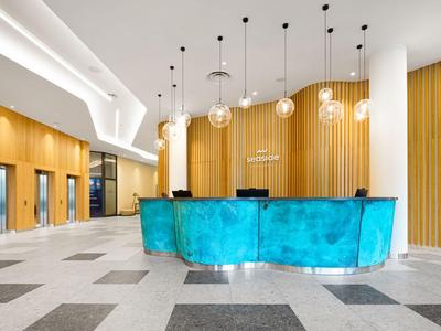 Nowoczesna recepcja hotelowa z turkusowym biurkiem i wiszącymi żarówkami.