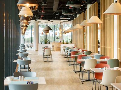 Jasna, nowoczesna restauracja z drewnianymi panelami i wieloma okrągłymi stolikami z krzesłami.