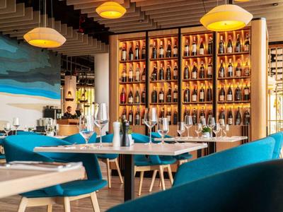 Nowoczesna restauracja z niebieskimi tapicerowanymi krzesłami i drewnianymi półkami pełnymi butelek wina