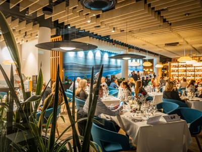 Nowoczesna restauracja z nakrytymi stołami i gośćmi przy ciepłym oświetleniu.