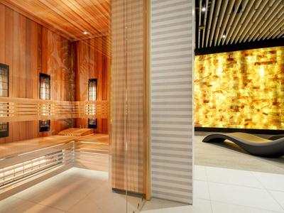 Área de spa moderna con sauna de madera e interior iluminado junto a un panel de pared amarillo.