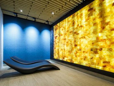 Sala de relajación moderna con dos tumbonas negras y una pared de piedra iluminada.