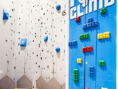 Pared de escalada colorida con elementos LEGO en un espacio interior con suelo de madera.