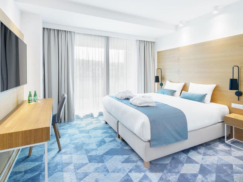 Habitación de hotel moderna con cama grande, cortinas claras, escritorio y alfombra azulada