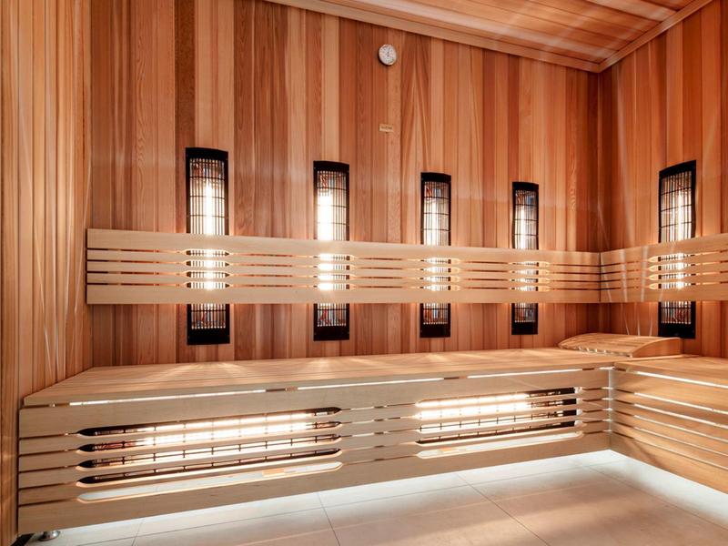 Sala de sauna con paredes de madera y bancos de doble nivel, iluminada con luz cálida.