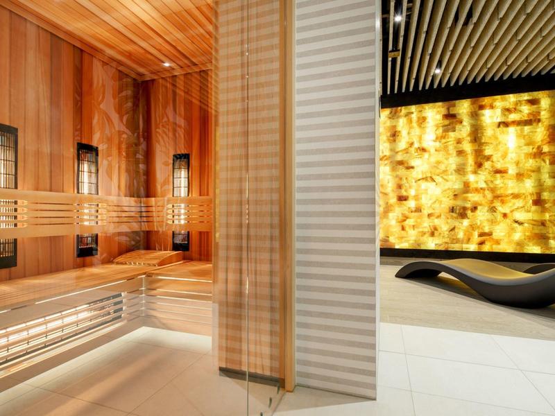 Área de spa moderna con sauna de madera e interior iluminado junto a un panel de pared amarillo.