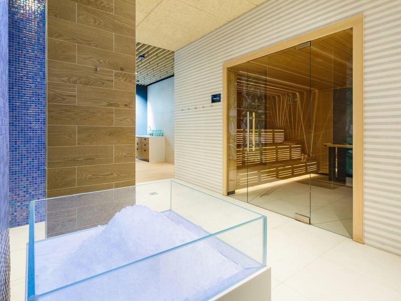 Área de sauna moderna con interior de madera y mampara de vidrio en una habitación luminosa