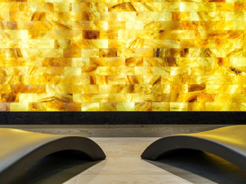 Dos tumbonas negras frente a una pared amarilla brillante en un área de spa.