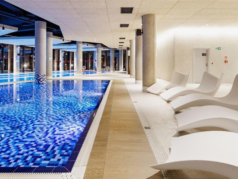 Piscina cubierta moderna con azulejos azules y tumbonas blancas a un lado en un hotel.