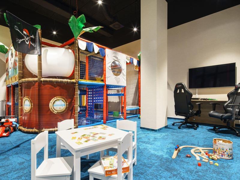 Espacio interior con alfombra azul, estructura de juego de barco pirata y mesa con sillas.