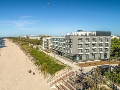 Hôtel moderne sur une large plage de sable avec ciel bleu clair et mer calme.