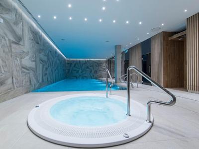 Area benessere moderna con vasca idromassaggio e piscina, circondata da dettagli in legno e pietra.