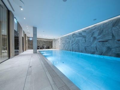 Piscina coperta moderna con acqua illuminata di blu e parete rocciosa nell'area spa