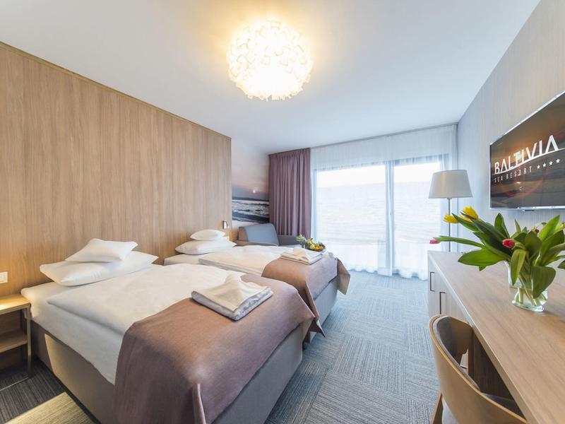 Chambre d'hôtel lumineuse avec deux lits simples, bureau, télévision et vue sur le balcon.