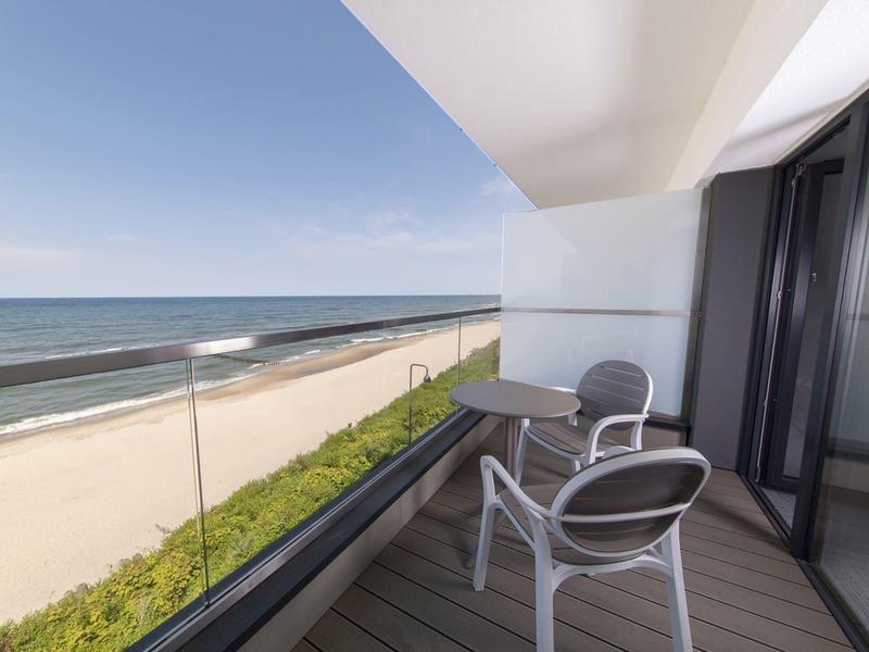 Balcon avec deux chaises donnant sur une plage de sable et la mer.