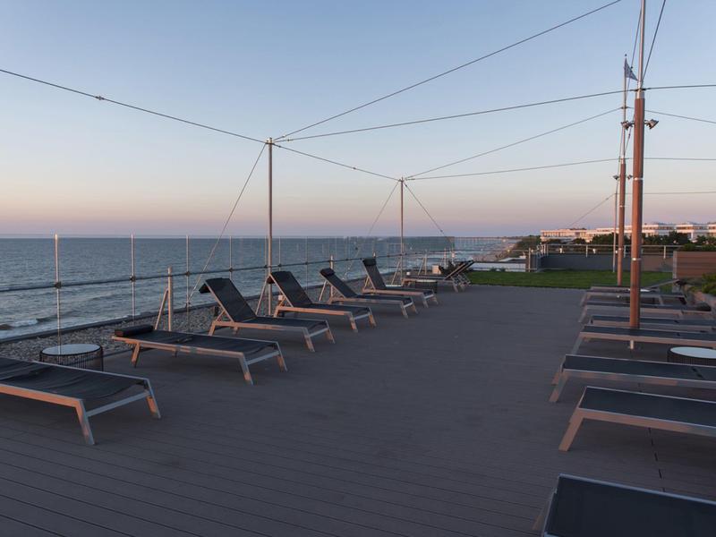 Chaises longues vides sur une terrasse avec vue sur la mer au coucher du soleil.