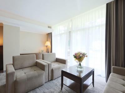 Sala luminosa con sillones grises, mesa de café de vidrio y ventana grande con cortinas.