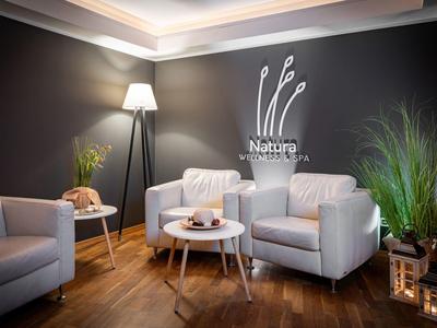 Acogedora zona del vestíbulo del hotel con sillones blancos, suelo de madera y plantas decorativas.