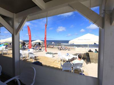 Vista desde una terraza cubierta hacia una playa de arena concurrida con sombrillas y personas junto al mar.
