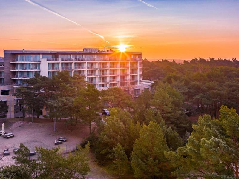 Un edificio moderno de hotel al atardecer, rodeado de árboles densos y cielo despejado.