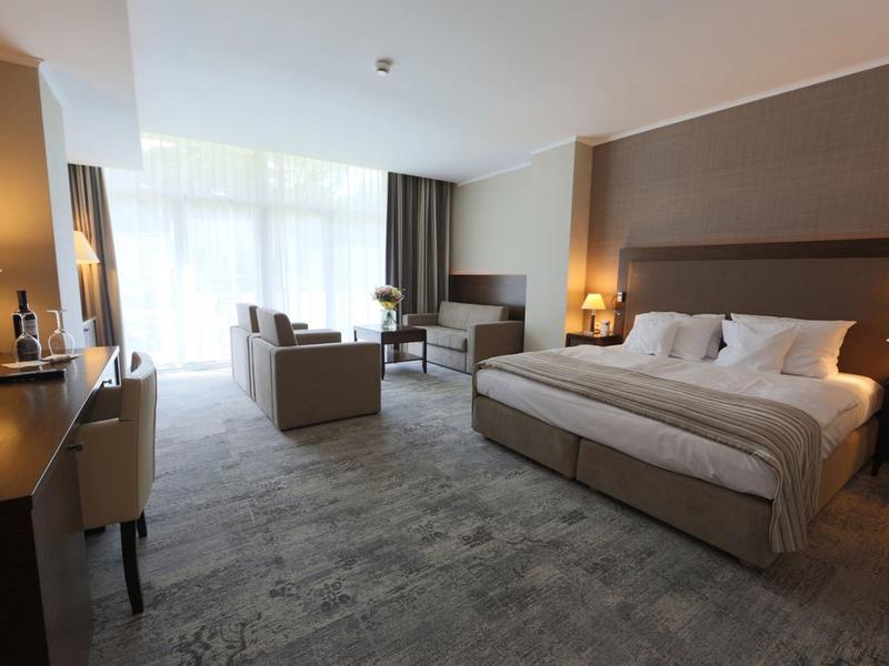 Habitación de hotel moderna con cama grande, zona de estar y ventana amplia que deja entrar luz natural.