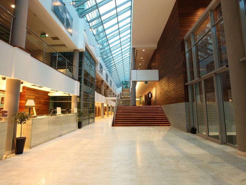 Moderna y luminosa recepción de hotel con techo de cristal y amplia escalera.