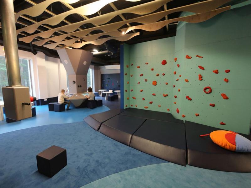 Moderna zona común de hotel con pared azul, muro de escalada y cojines coloridos.