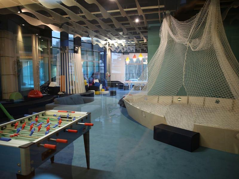 Salón moderno con futbolín, zona de asientos y red decorativa en el techo.