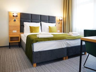 Gemütliches Hotelzimmer mit großem Bett, grüner Bettdecke und moderner Einrichtung.