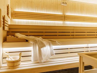 Helle Sauna mit Holzliegen, einem weißen Handtuch und einem Holzeimer mit Kelle.