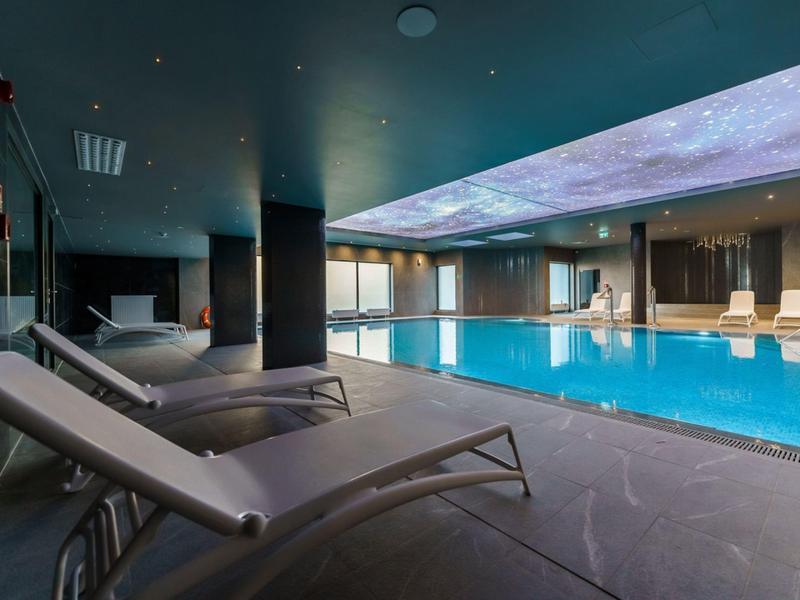 Modernes Hallenbad mit Liegestühlen und indirekter Beleuchtung an der Decke.