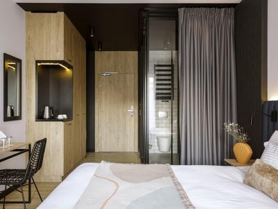 Nowoczesny pokój hotelowy z łóżkiem, biurkiem, krzesłem i szafą w stonowanych kolorach.