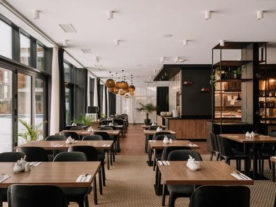 Nowocześnie urządzona sala restauracyjna hotelu z stołami i krzesłami w ciepłych kolorach.