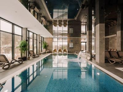 Nowoczesny kryty basen z leżakami i dużymi oknami wpuszczającymi dużo światła dziennego.