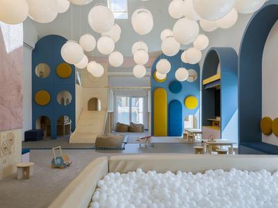 Nowoczesne wnętrze z wiszącymi kulistymi lampami, basenem z kulkami i zabawnymi elementami architektonicznymi.